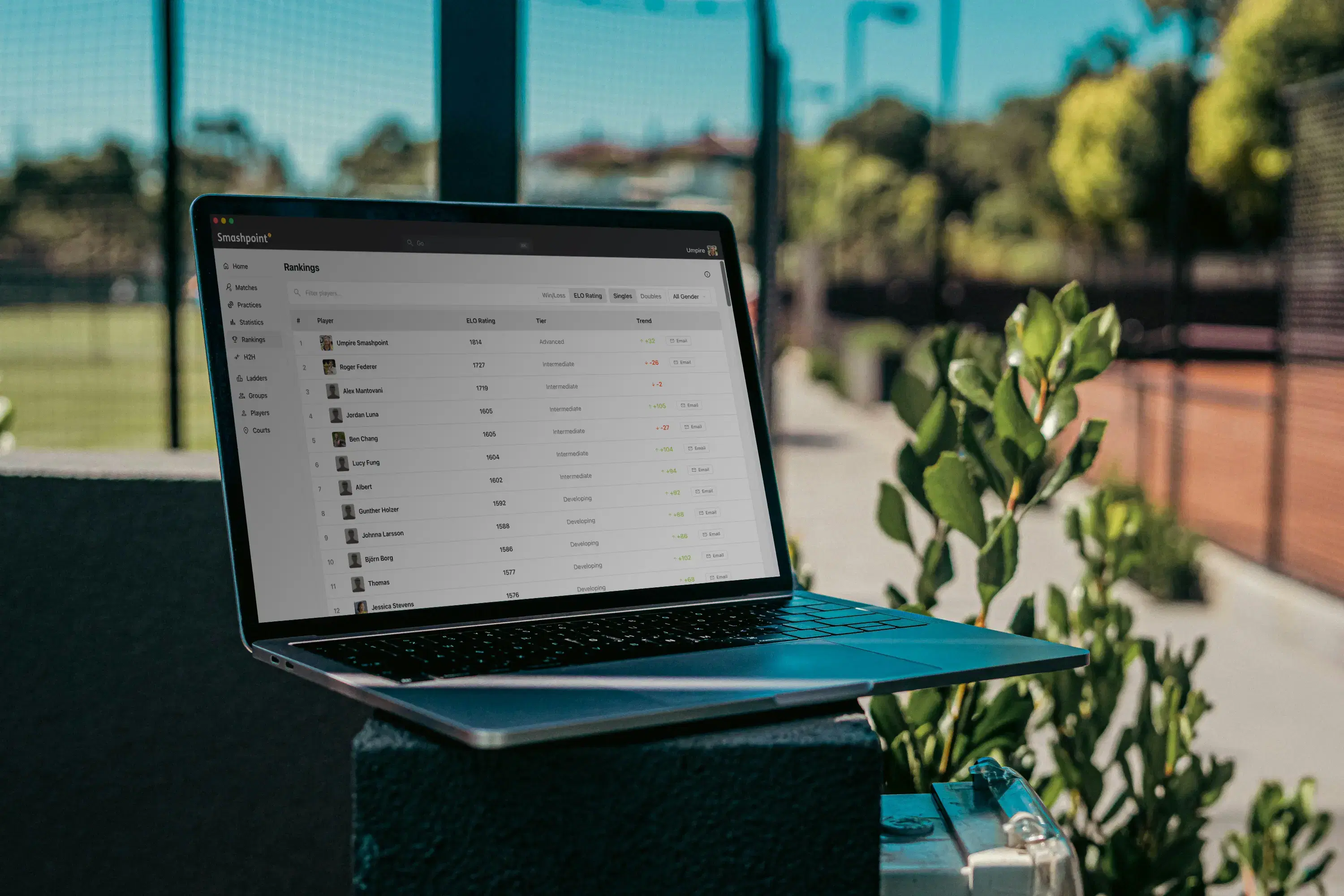 A laptop showing the Smashpoint rankings dashboard on a club patio beside the courts